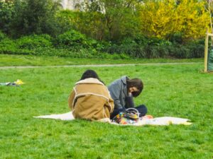 A family spreads out a picnic blanket on the grass in one of London's sunny parks on a summer afternoon