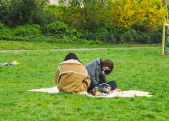A family spreads out a picnic blanket on the grass in one of London's sunny parks on a summer afternoon