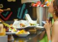 A woman sampling street food at a busy London neighbourhoods market, surrounded by global food stalls