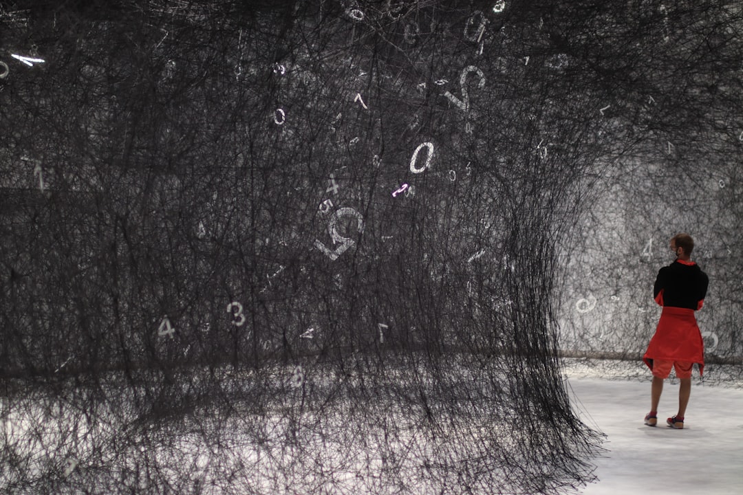 A woman examines a dark void installation by Anish Kapoor, surrounded by the concrete walls of a contemporary gallery