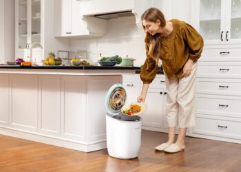A woman carefully sorting household waste into recycling bins in a small London flat kitchen
