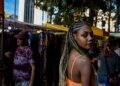 black-woman-market-vendor-unsplash - LONDONwebzine A Ghanaian community market trader in London arranges traditional fabric and food at an outdoor stall