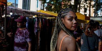 black-woman-market-vendor-unsplash - LONDONwebzine A Ghanaian community market trader in London arranges traditional fabric and food at an outdoor stall