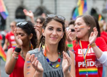 A joyful crowd of people waving rainbow flags during Pride in London along the parade route