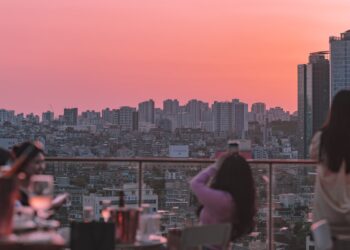 A woman enjoying cocktails at one of London's rooftop bars with the city skyline in the background on a summer evening.