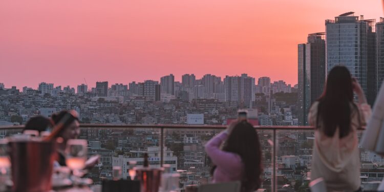 people-in-rooftop-cocktail-party-unsplash - LONDONwebzine A woman enjoying cocktails at one of London's rooftop bars with the city skyline in the background on a summer evening.