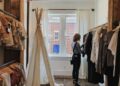 Une femme parcourt attentivement un rail curé de vêtements slow fashion à l'intérieur d'une petite boutique londonienne