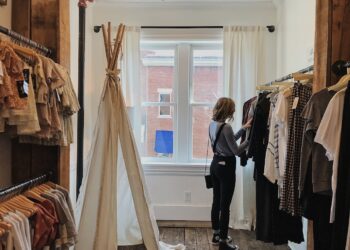 A woman carefully browsing a curated rail of slow fashion garments inside a small London boutique