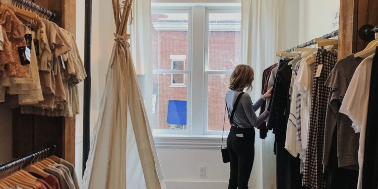 woman-browsing-ethical-boutique-rails-unsplash - LONDONwebzine A woman carefully browsing a curated rail of slow fashion garments inside a small London boutique