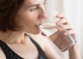 A woman starting her morning routine with a glass of water before the London heat builds outside her window