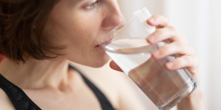 A woman starting her morning routine with a glass of water before the London heat builds outside her window