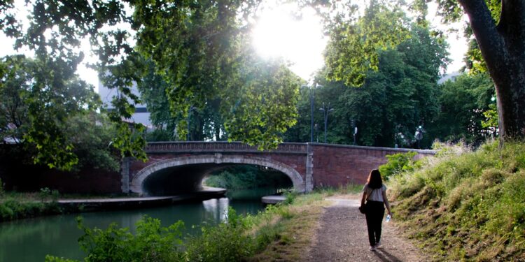woman-walking-canal-path-unsplash - LONDONwebzine A woman walks along London's canal towpaths on a sunny summer morning with narrowboats moored behind her