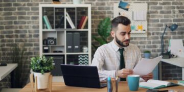 business-owner-reviewing-lease-documents-unsplash - LONDONwebzine A business owner carefully reviewing a commercial lease agreement in a bright London studio space