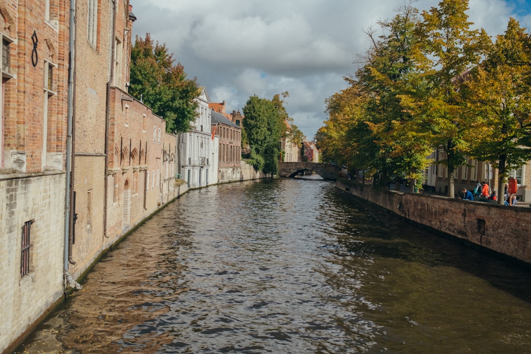 A couple walking along a Bruges canal on a city break from London, with medieval buildings reflected in the water