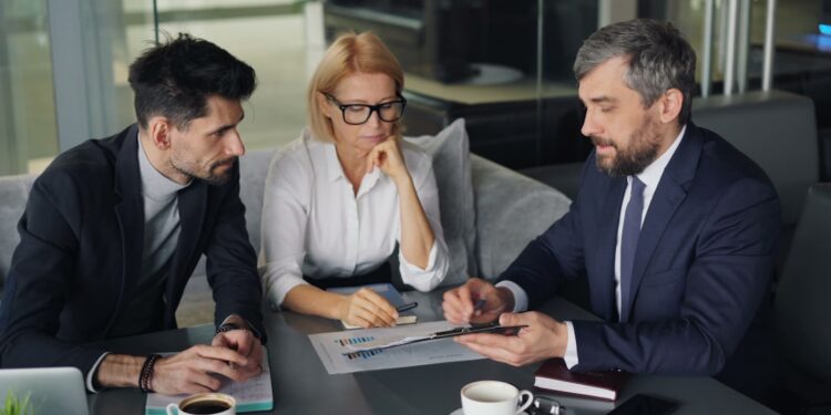 financial-advisor-client-meeting-with-stocks-in-the-back-unsplash - LONDONwebzine A financial advisor in a London office explains how to open a stocks ISA to a client across the desk