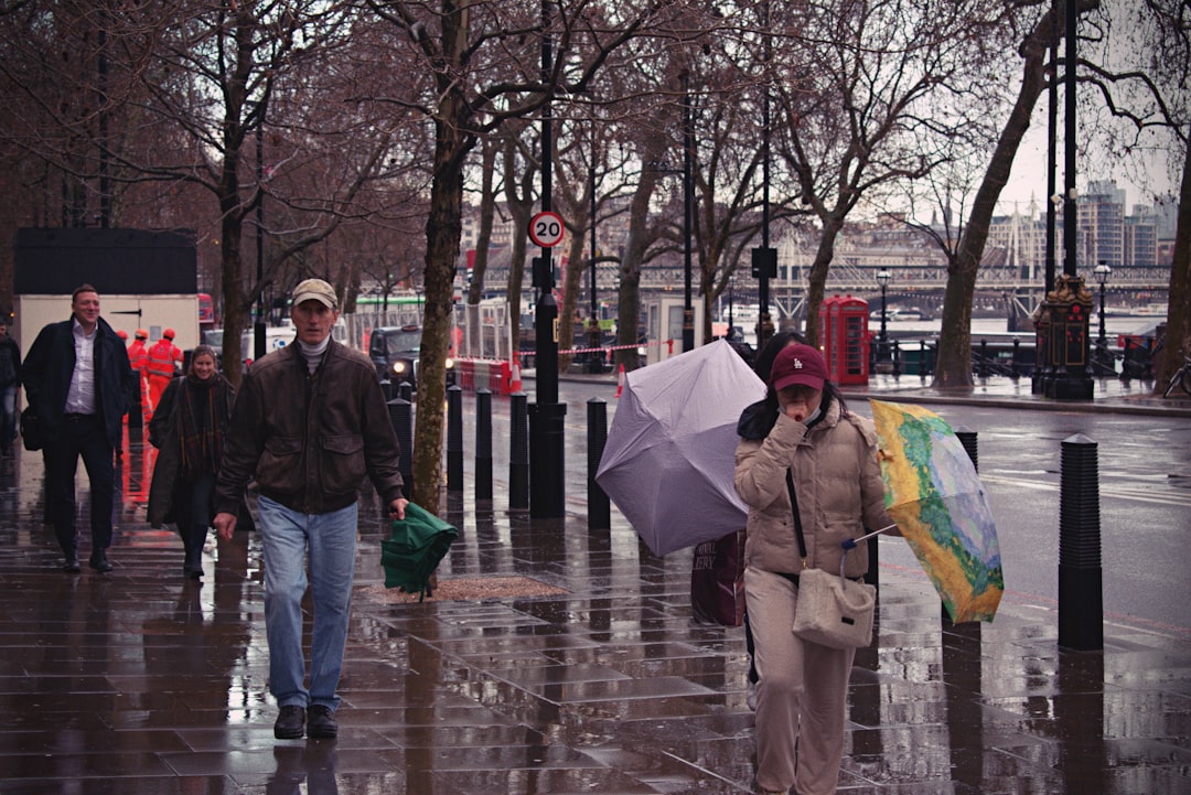 Two people walk through a London shower with umbrellas, dressed for practical August wear with a waterproof outer layer.