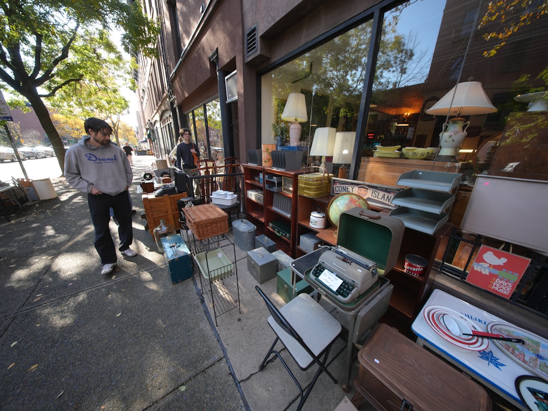 A man examining a wood side table at a London market, choosing pieces to furnish rental flat without breaching his tenancy.