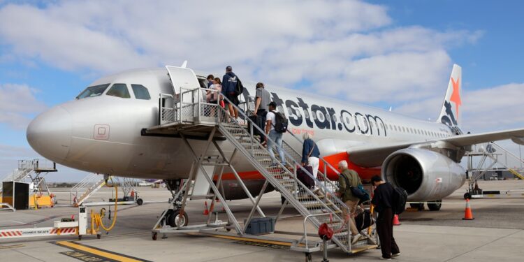 A woman with a suitcase boarding at a London airports rail connection, with signage visible in the background.