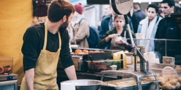A vendor hands a customer fresh street food at Borough Market, one of London's most celebrated street food destinations.