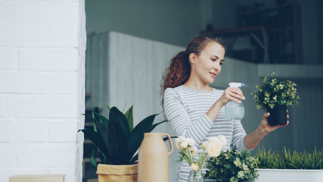 A woman placing potted plants on a sunny windowsill in her flat, using greenery and natural light to create a warm home.
