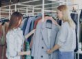 woman-browsing-clothes-unsplash - LONDONwebzine A woman smiling while browsing colourful rails in a London charity shop, looking for secondhand summer pieces