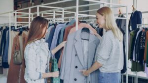 A woman smiling while browsing colourful rails in a London charity shop, looking for secondhand summer pieces