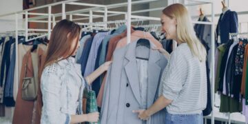 woman-browsing-clothes-unsplash - LONDONwebzine A woman smiling while browsing colourful rails in a London charity shop, looking for secondhand summer pieces