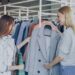 woman-browsing-clothes-unsplash - LONDONwebzine A woman smiling while browsing colourful rails in a London charity shop, looking for secondhand summer pieces