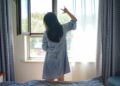 A woman standing by a bright London window in the morning, building a healthy sleep routine through early light exposure