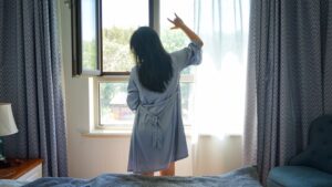 A woman standing by a bright London window in the morning, building a healthy sleep routine through early light exposure