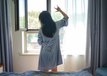 A woman standing by a bright London window in the morning, building a healthy sleep routine through early light exposure