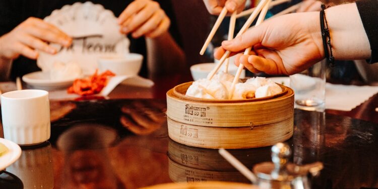 woman-eating-dumplings-restaurant-unsplash - LONDONwebzine A woman smiling while sharing dim sum dishes with friends at a London Cantonese restaurant