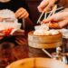 woman-eating-dumplings-restaurant-unsplash - LONDONwebzine A woman smiling while sharing dim sum dishes with friends at a London Cantonese restaurant