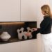 A woman arranging vases on freestanding shelves in a bright London flat, showing how to personalise a rented space.