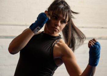 A woman wrapping her hands before her first session at a boxing gym in London, preparing to train with a coach nearby