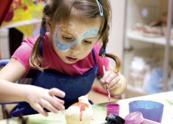 A young child concentrating on a pottery wheel during kids workshops in London, guided by an art instructor in a studio.
