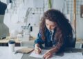 woman-designer-sustainable-fabric-studio-unsplash - LONDONwebzine A designer examines deadstock fabric in a studio, representing the sustainable fashion movement at London Fashion Week.