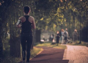 A smiling woman joins a running club group in a London park during autumn, wearing a light jacket and trainers.