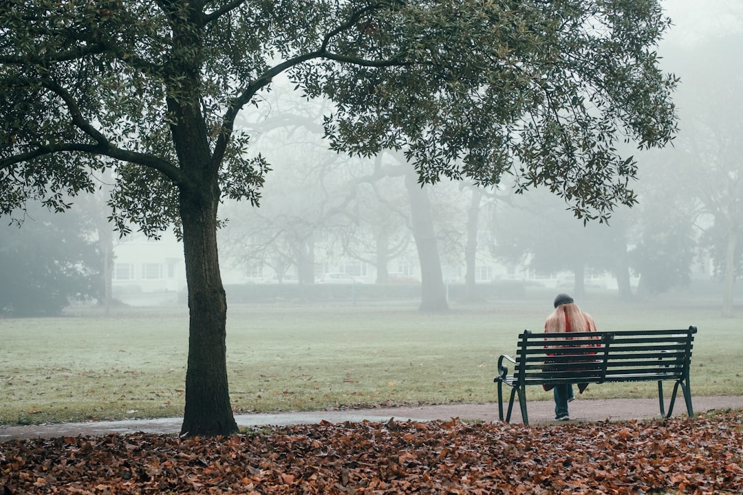 A woman writing in a notebook on a park bench as part of her morning routine in a London park in early autumn