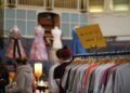 womn smiling as she browses a clothing rail at vintage fairs in London, surrounded by pre-loved coats and jackets.