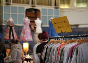 womn smiling as she browses a clothing rail at vintage fairs in London, surrounded by pre-loved coats and jackets.