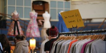 women-browsing-vintage-clothing-rail-unsplash - LONDONwebzine womn smiling as she browses a clothing rail at vintage fairs in London, surrounded by pre-loved coats and jackets.