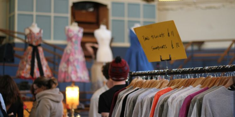 women-browsing-vintage-clothing-rail-unsplash - LONDONwebzine womn smiling as she browses a clothing rail at vintage fairs in London, surrounded by pre-loved coats and jackets.