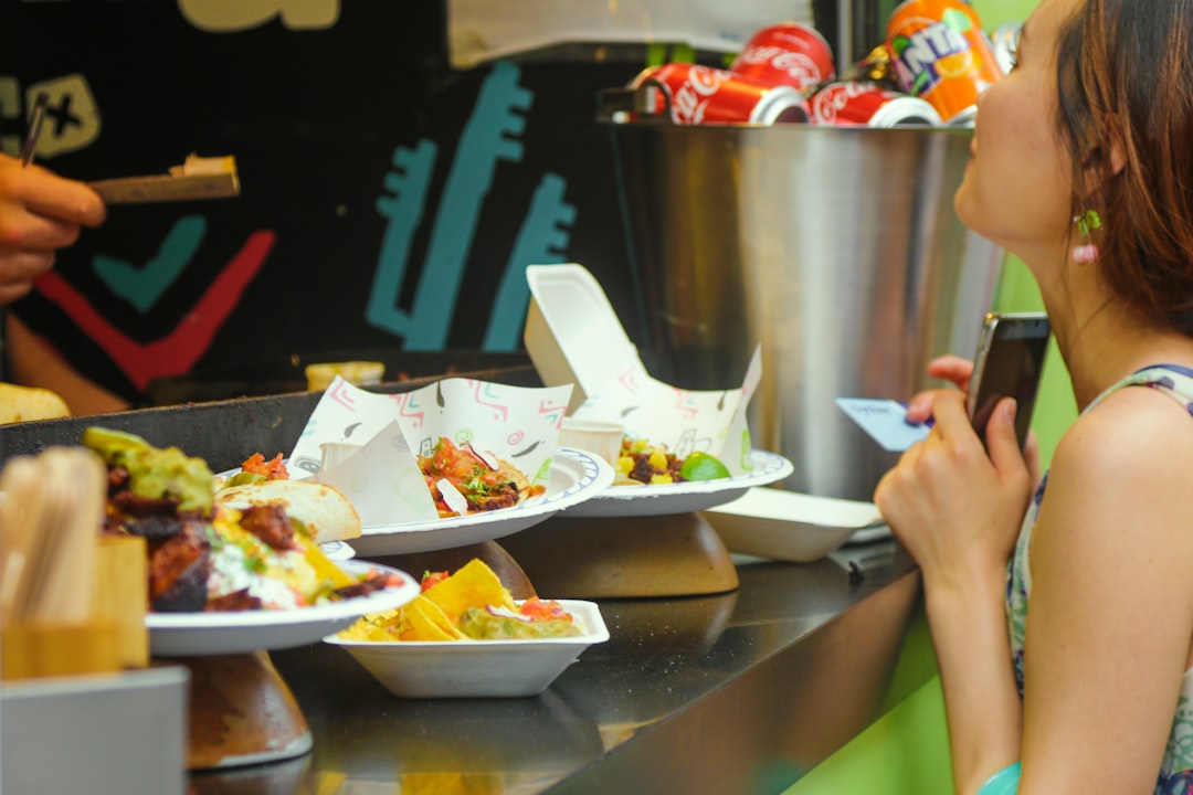 Una mujer probando comida callejera en un mercado abarrotado de barrios londinenses, rodeada de puestos de comida global