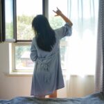 A woman standing by a bright London window in the morning, building a healthy sleep routine through early light exposure