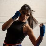 A woman wrapping her hands before her first session at a boxing gym in London, preparing to train with a coach nearby