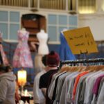 womn smiling as she browses a clothing rail at vintage fairs in London, surrounded by pre-loved coats and jackets.